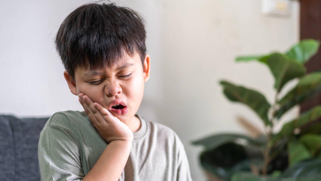 Seorang anak sedang menahan nyeri sakit gigi.