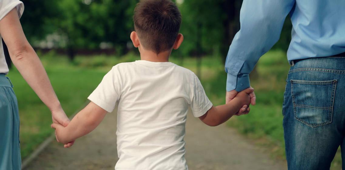 Seorang anak bergandengan tangan dengan kedua orang tuanya